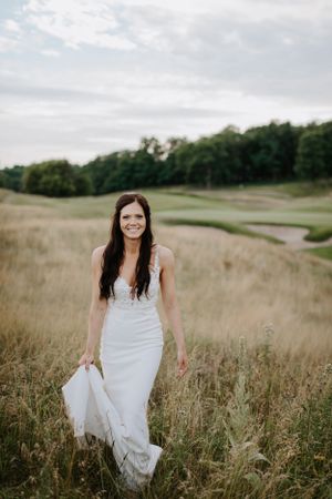 White wedding dress flowing in a rustic field of tall grass on a cloudy day.