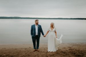 Newlyweds walking along a scenic beach shoreline at sunset.