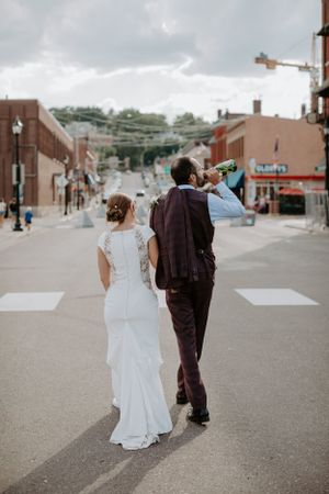 A couple in wedding attire walking together on an urban street with buildings in the background.