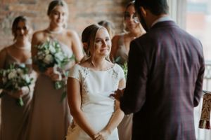 An intimate wedding ceremony moment with bridesmaids in soft neutral dresses watching the exchange of vows.