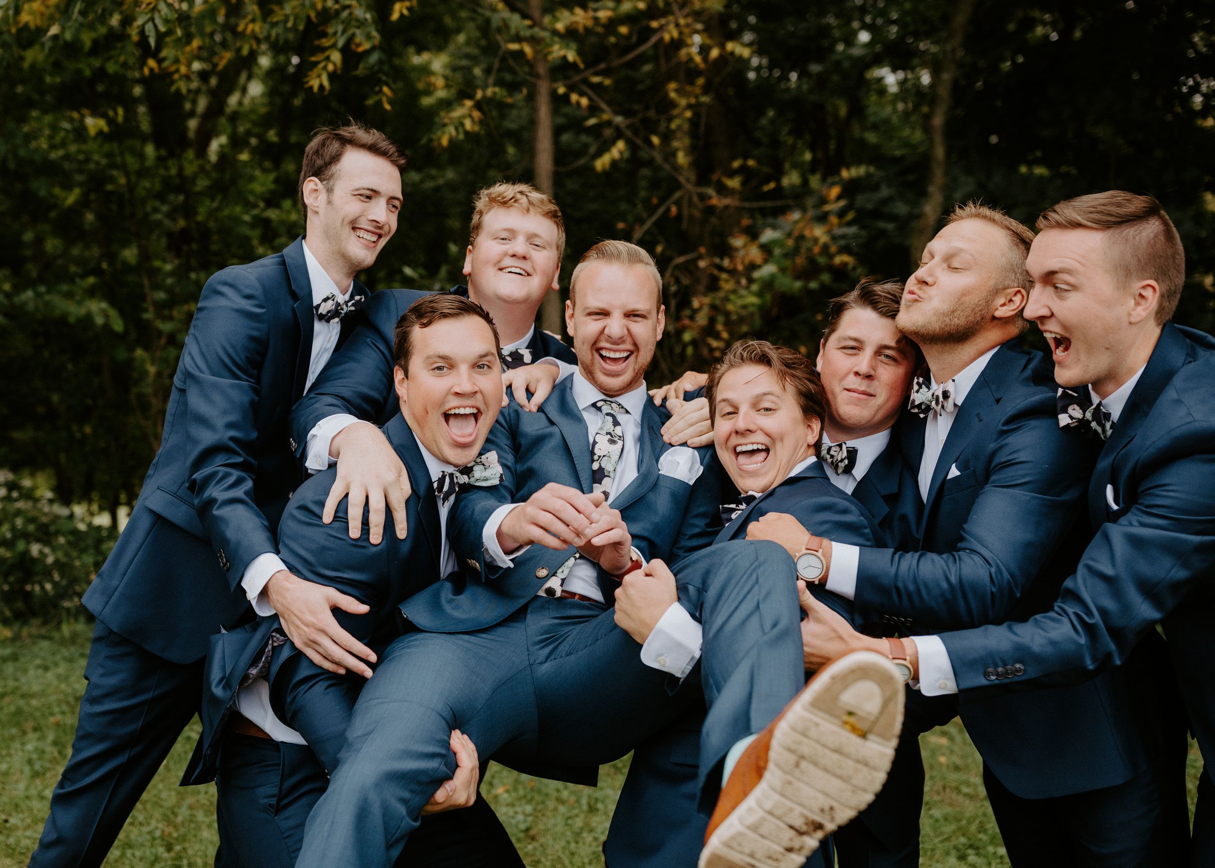 Groomsmen in navy suits posing playfully for group photo outdoors.