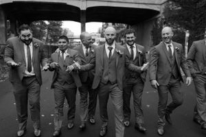 Groomsmen in dark suits walking in formation down a city street.