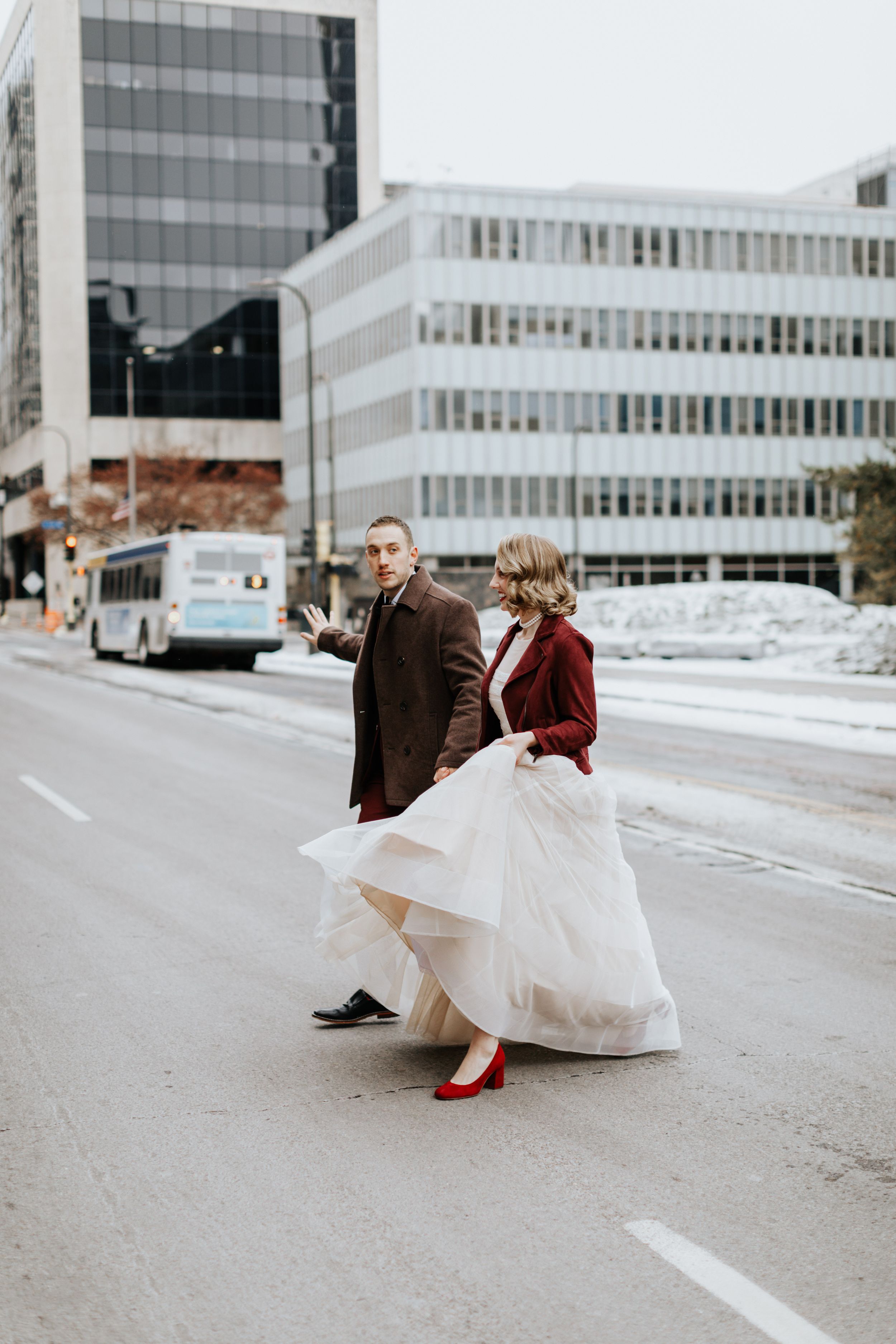 Wedding couple strolls through city street with white dress flowing in wind.