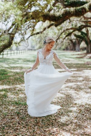 A white wedding dress twirls gracefully on a path beneath Spanish moss-covered trees.