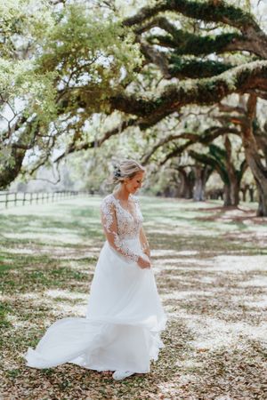 A flowing white wedding gown with lace sleeves captures movement under moss-draped oak trees.