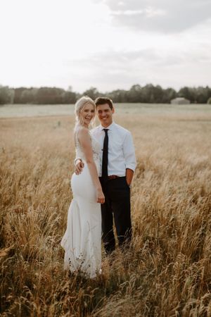 Wedding couple posing together in a golden wheat field during sunset.