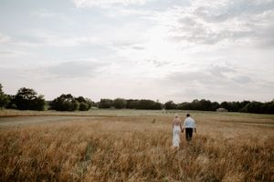 Panoramic view of a couple walking through a golden field under cloudy skies.