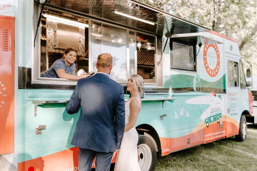 A couple stands by a vintage-style food truck with mint and coral accents.