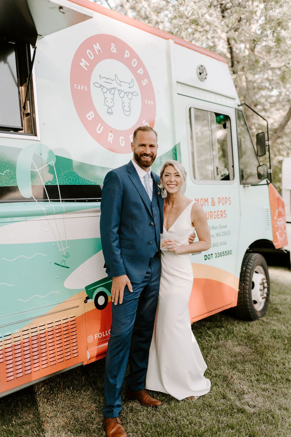 A couple poses in front of a mint green and coral food truck at an outdoor event.