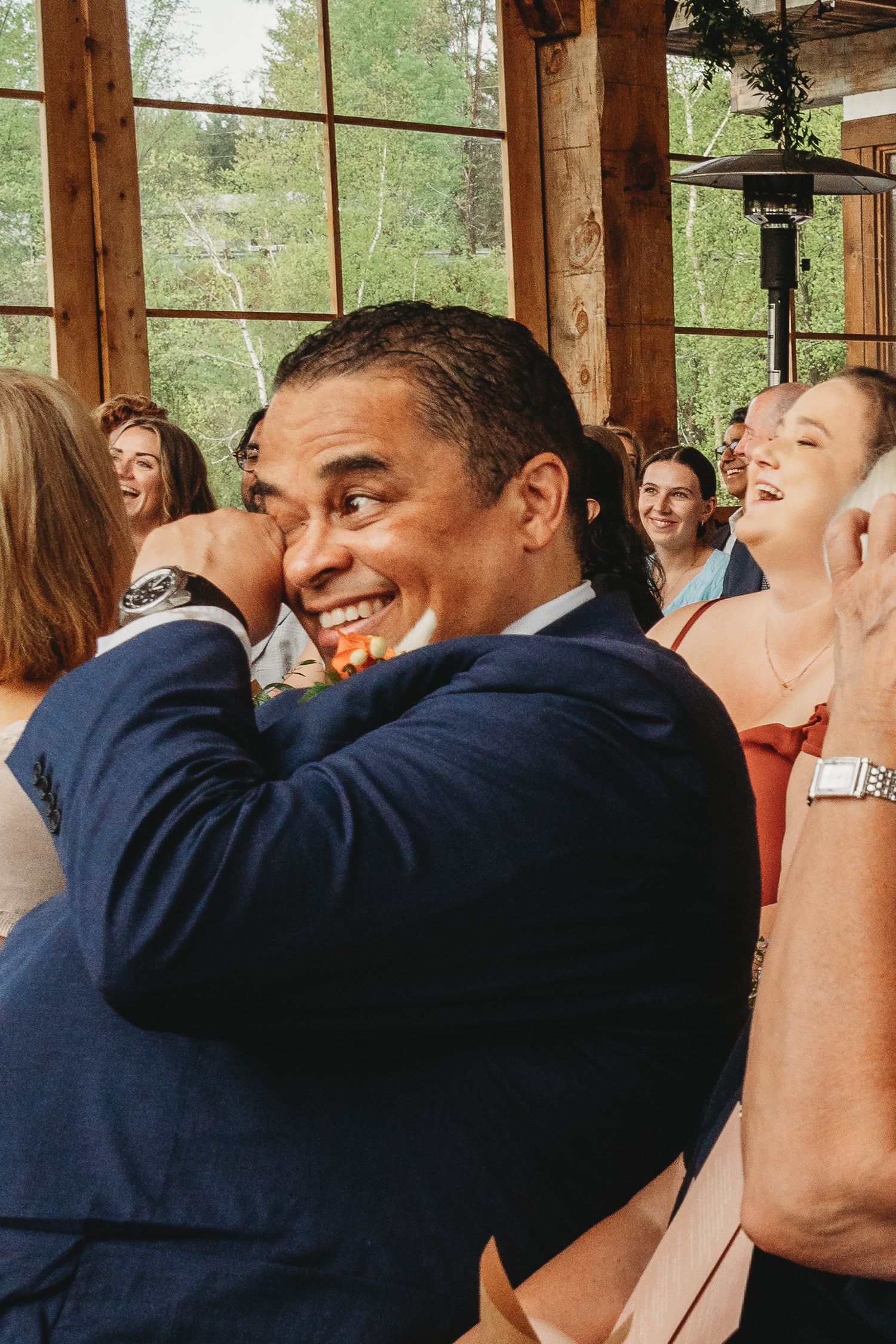 Wedding guest in navy suit shares a joyful laugh during ceremony.