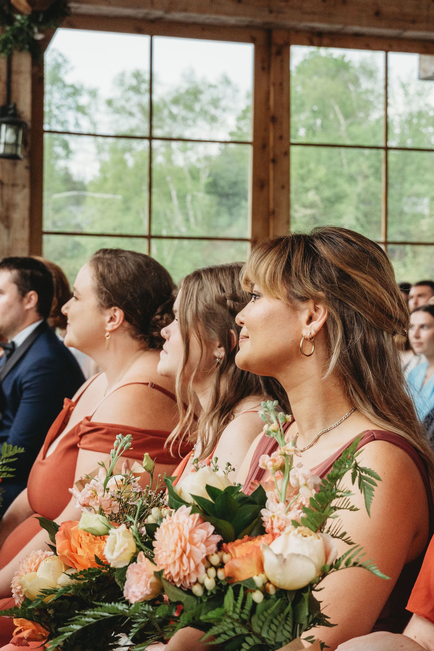 Bridesmaids in coral dresses holding floral bouquets with peach and orange blooms at wedding ceremony.