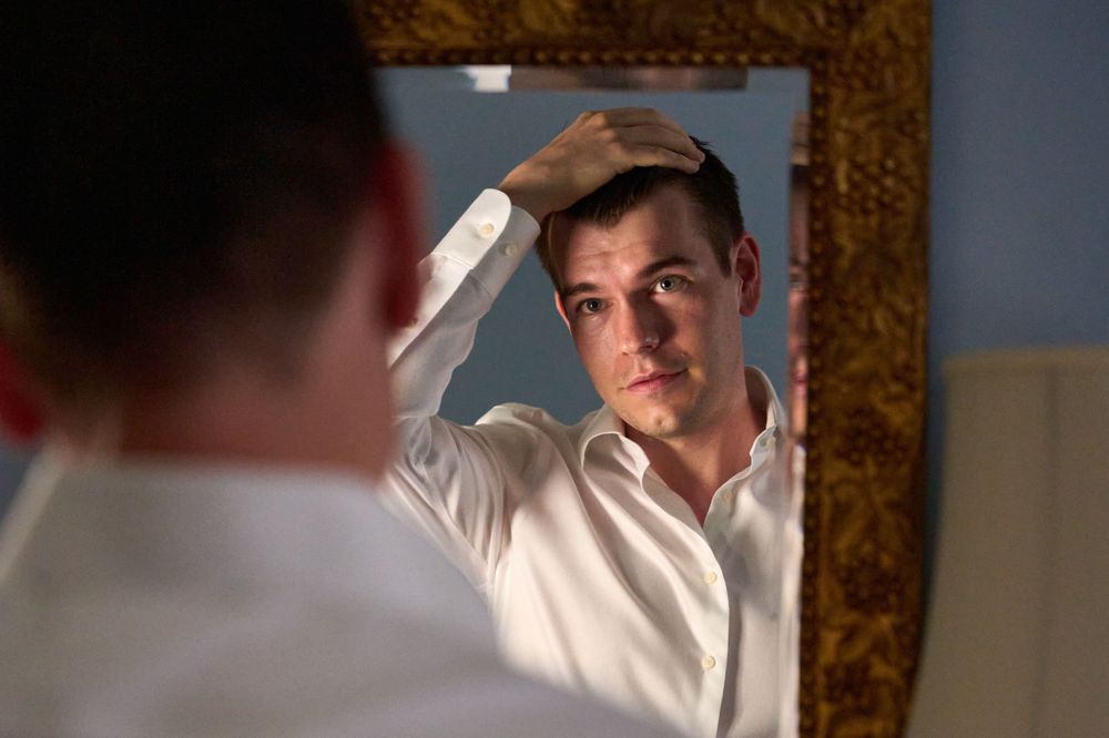 Dark haired young groom checks his mirrored reflection