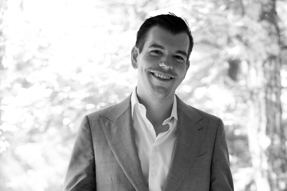 Handsome dark haired groom smiles in woodland setting