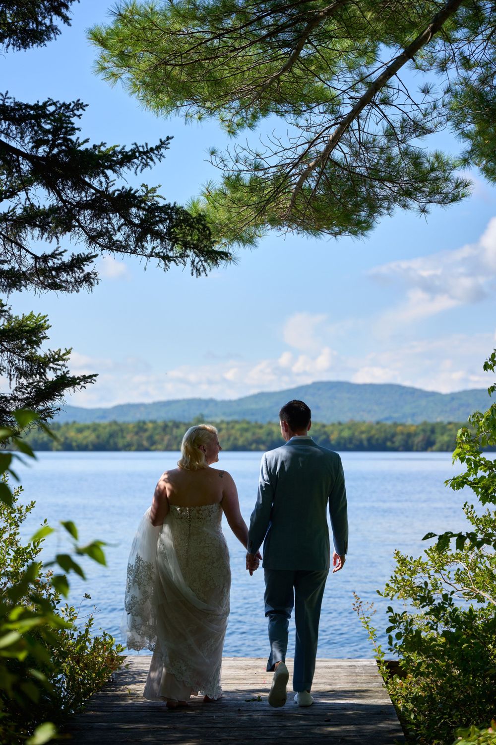 Blue skies and blue waters of Squam Lake frame hand in hand bride and groom