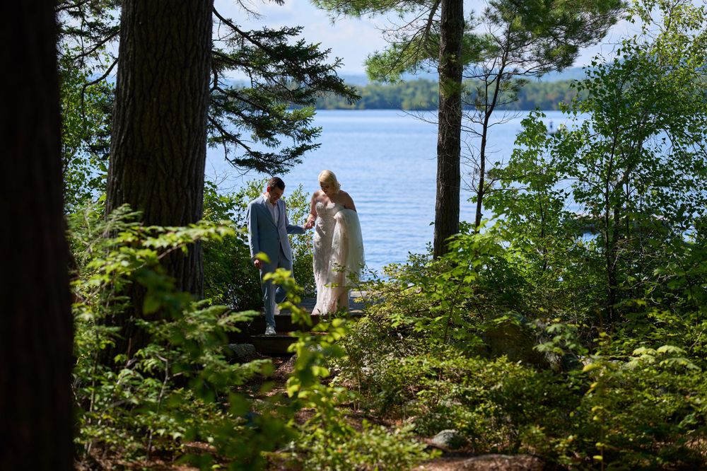 Large trees by the shore of Squam Lake frame bride and groom