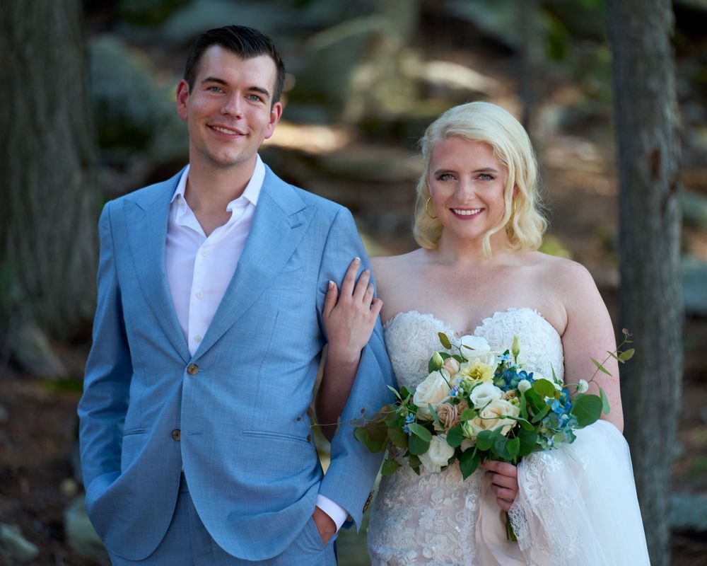 Close up three quarter view of blue suited groom and white gowned bride clasping bouquet