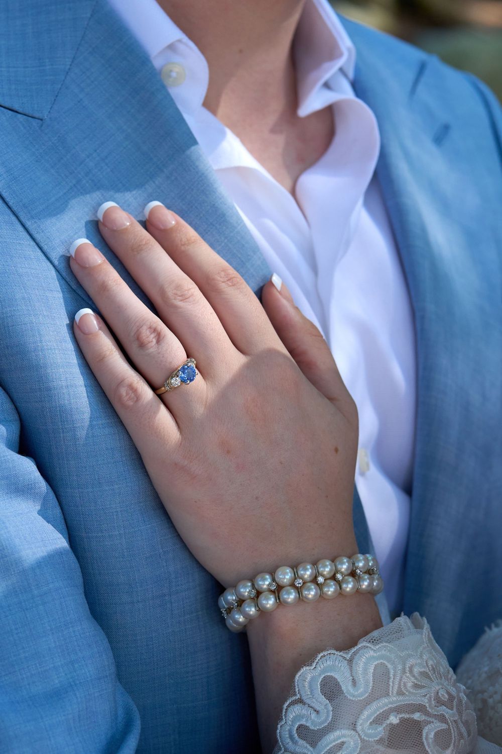 Bride rests her bejeweled hand on the sky blue lapel of her groom