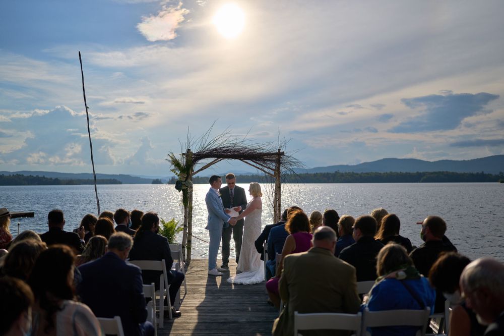 Full western sun illuminates arbor, wedding ceremony, and guests on Squam Lake pier