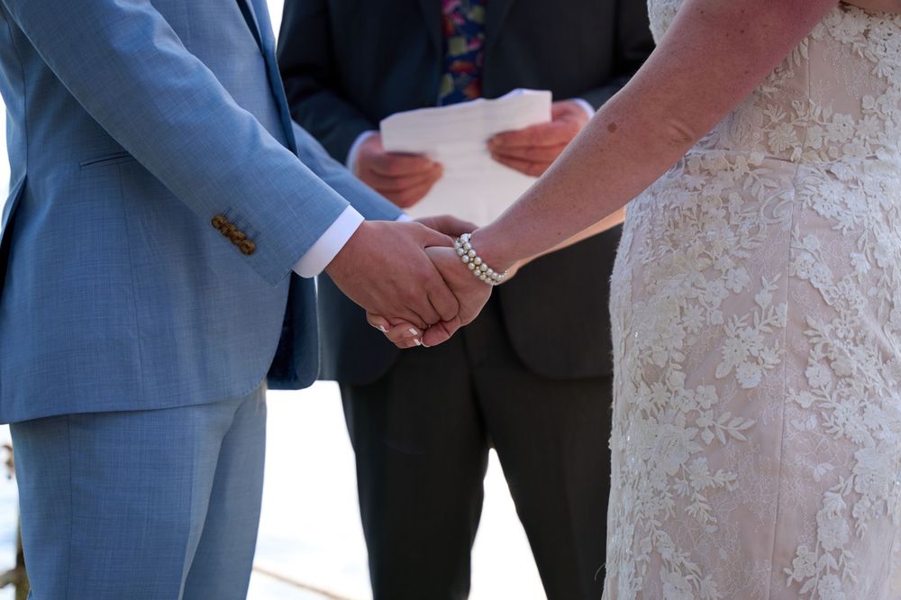 During Squam Lake wedding ceremony bride and groom clasp hands as officiant speaks