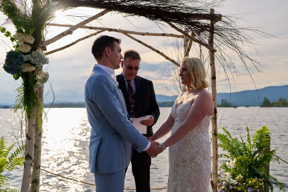 Bride and groom exchange vows beneath lakeside arbor