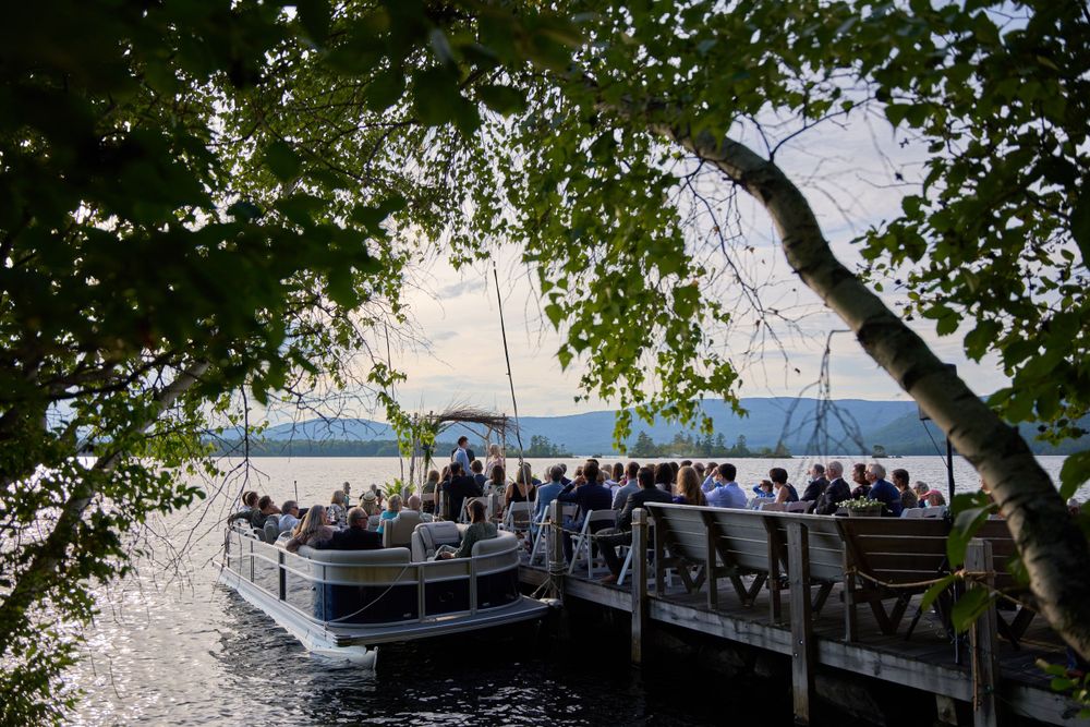 Wedding guests fill pontoon boat docked beside seated guests on Squam Lake pier