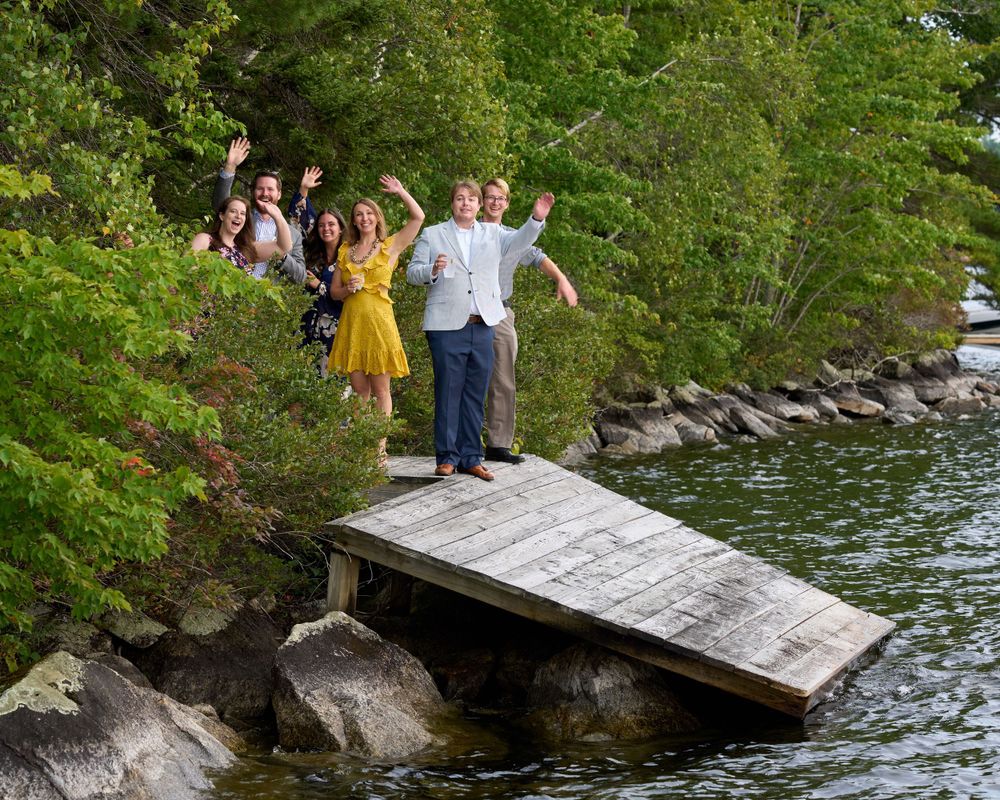 A small group of lakeside wedding guests wave and cheer with exuberance
