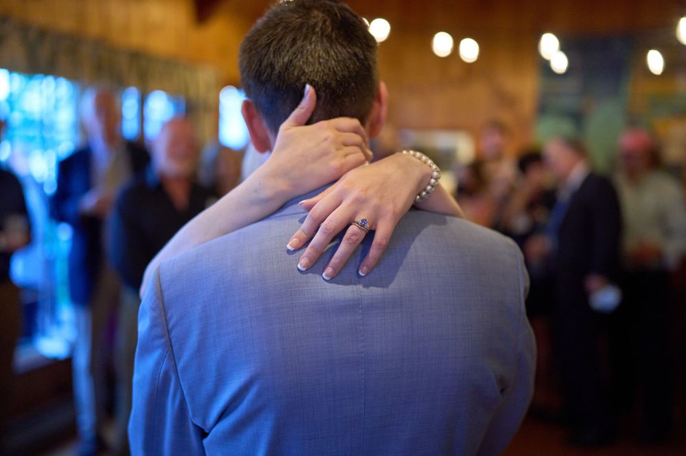 Bride clasps her hands around the blue suited back of groom during first dance