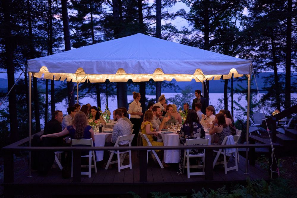 Wedding guests enjoy dinner under gaily lit tent canopy Squam Lake