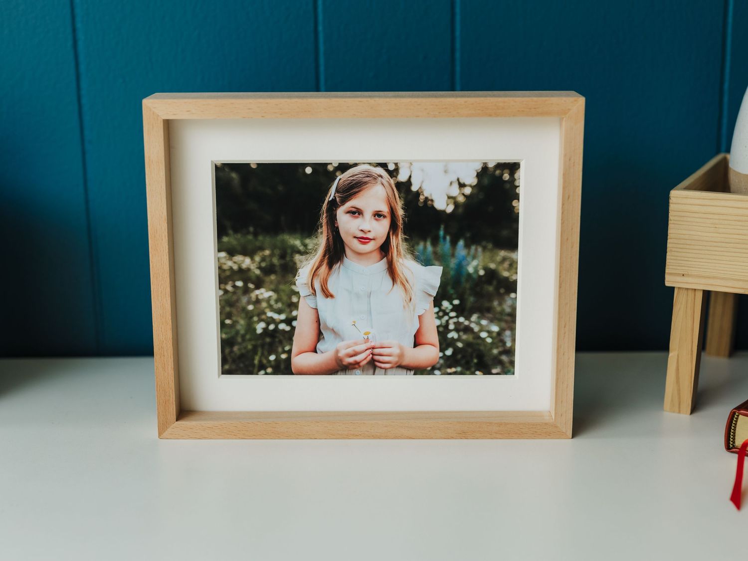 A framed portrait photo displayed on a white surface against a teal wall.