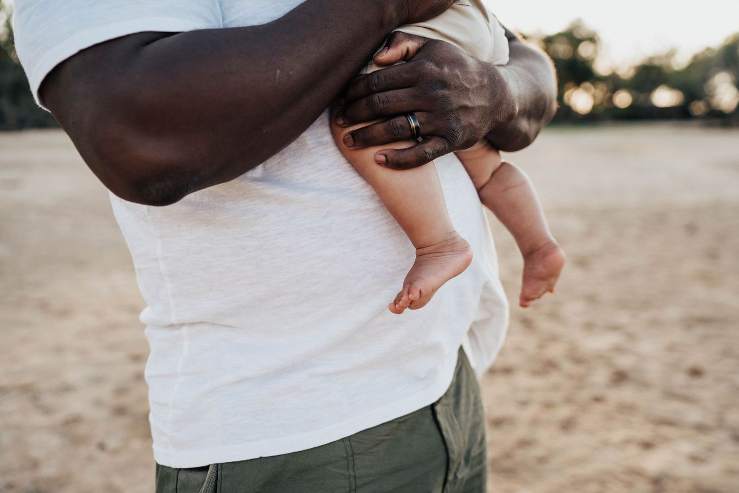 Close-up of hands holding baby's feet on sandy beach.