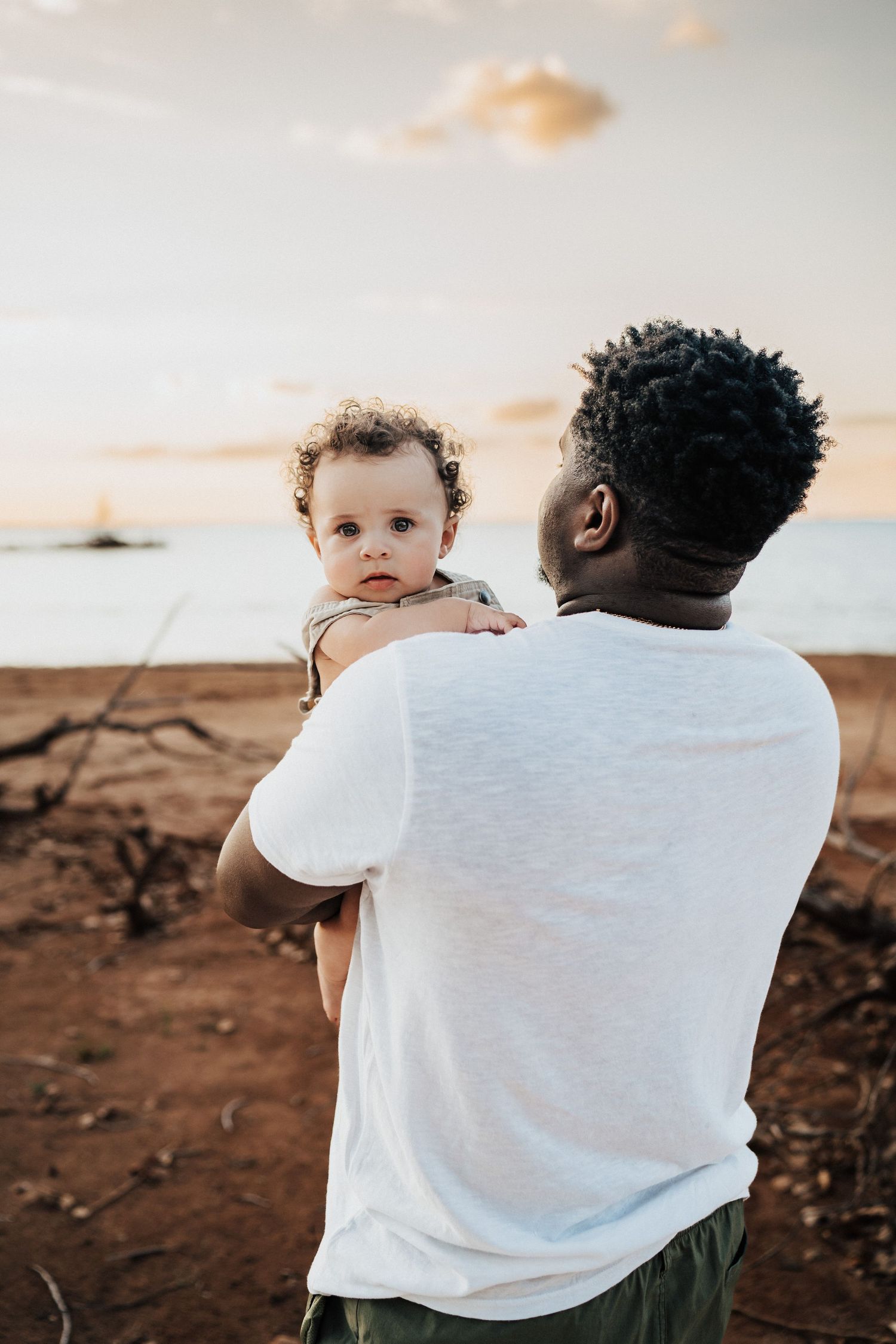 Parent holding toddler against sunset sky backdrop.