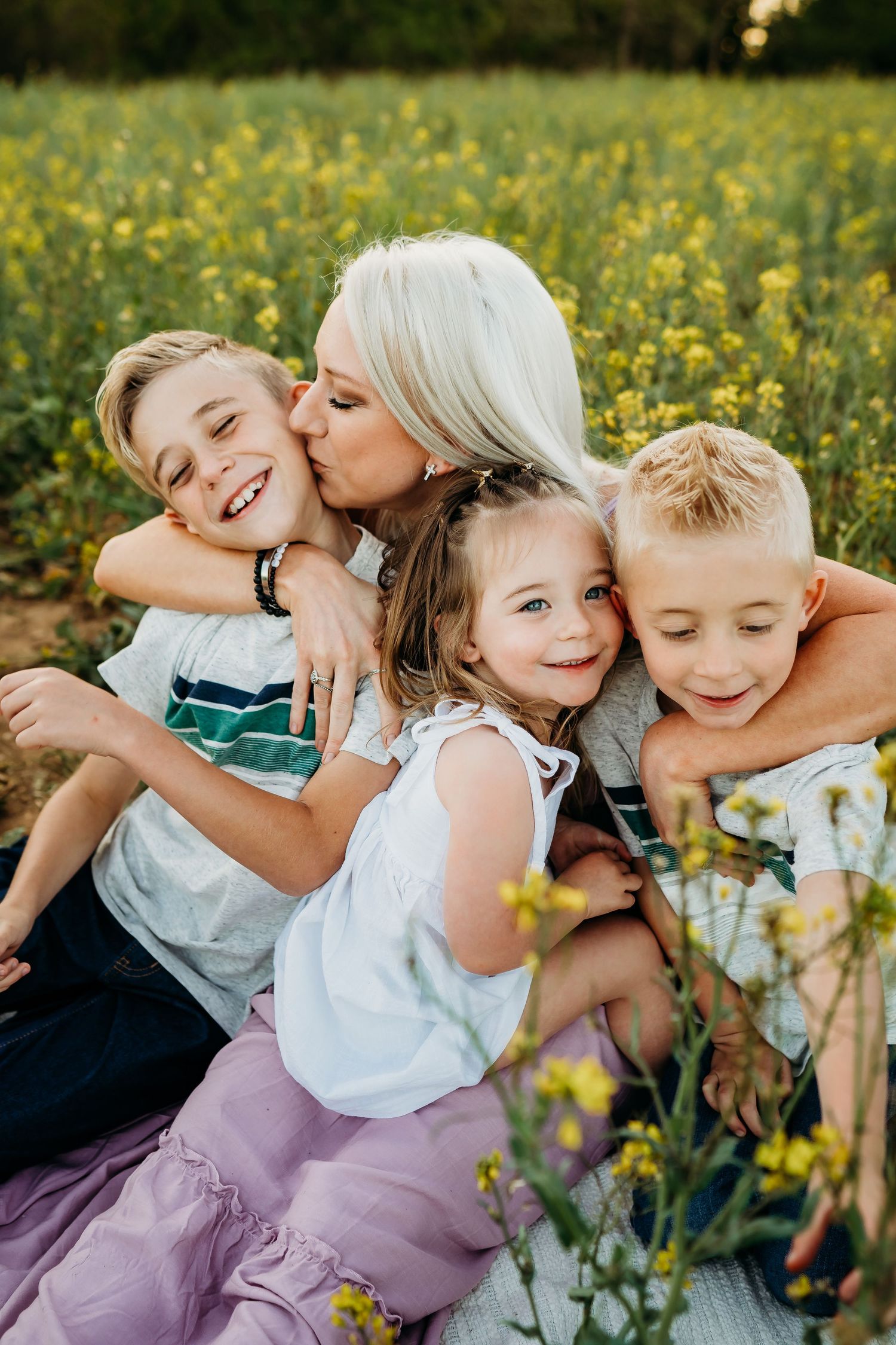 Loving family portrait taken in a field of yellow wildflowers during golden hour.