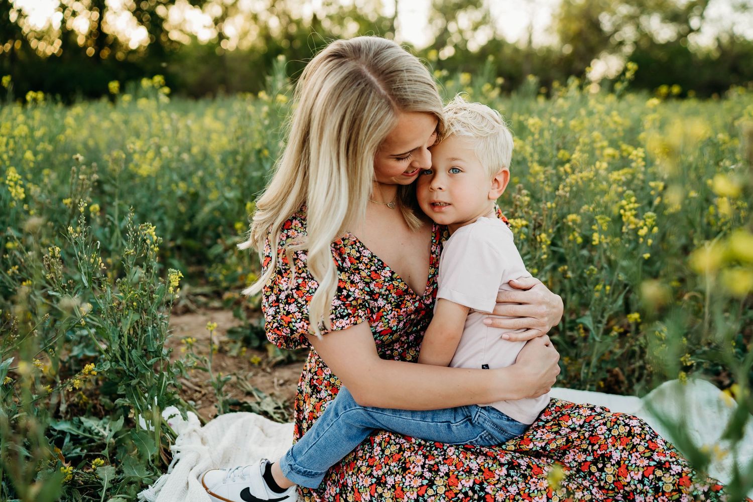 Mother and child share tender moment in field of yellow wildflowers at sunset.