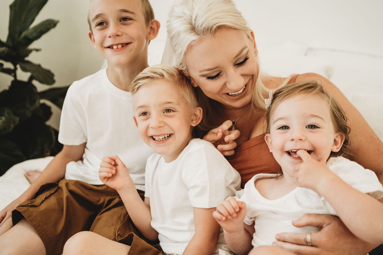 Family with children laughing together on white bed during casual lifestyle photoshoot.