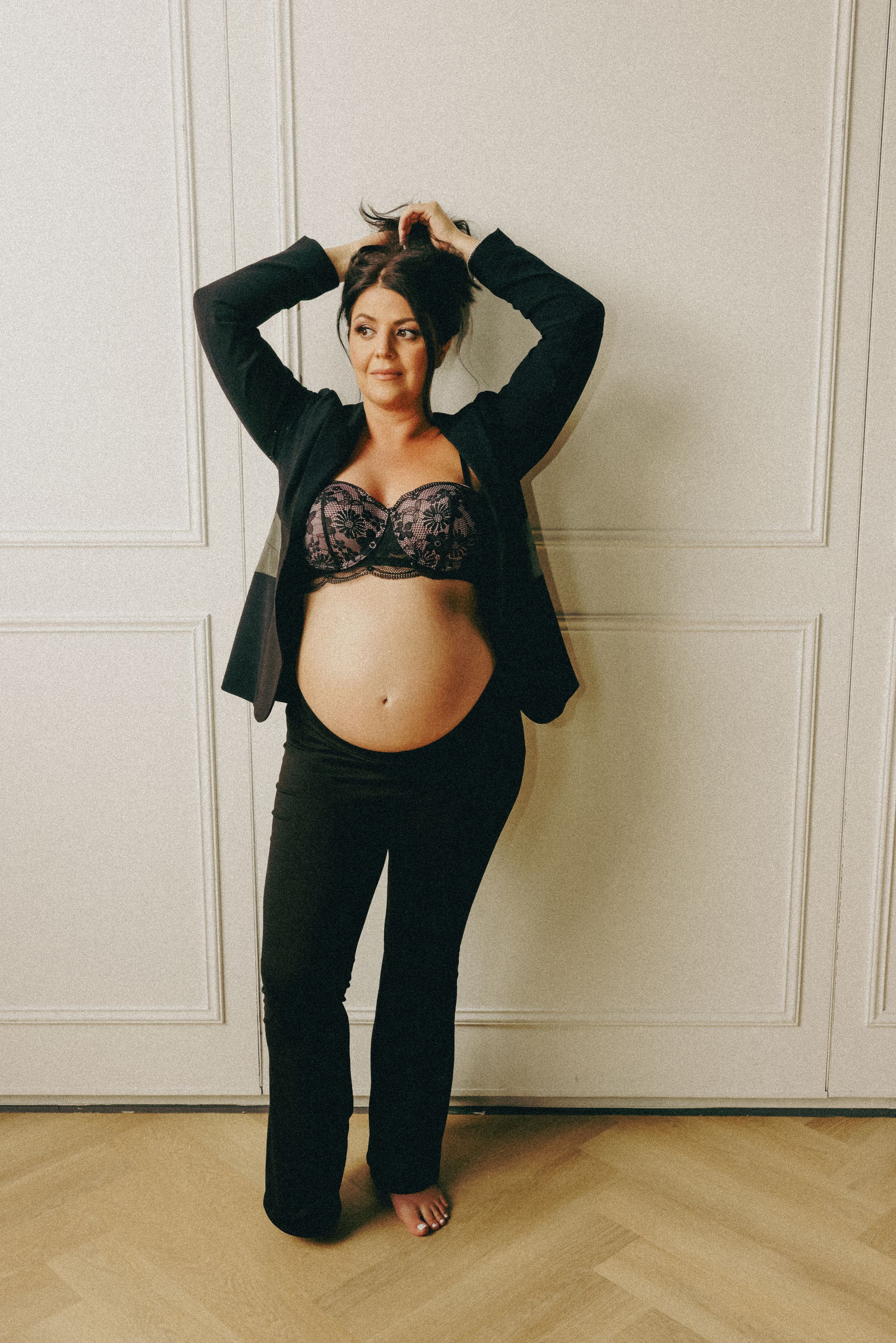 A maternity portrait in casual black attire against a minimalist white background.