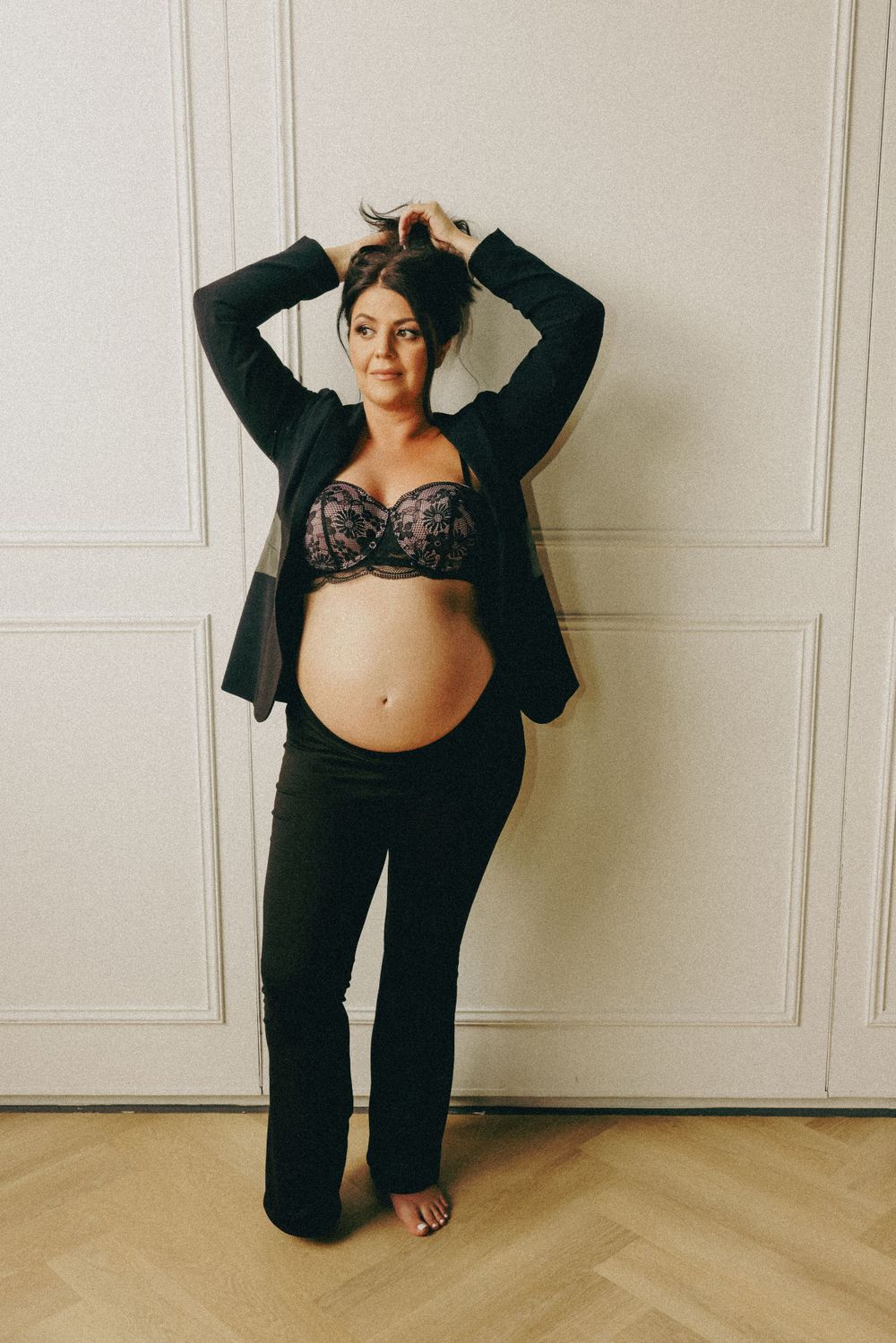 A maternity portrait in casual black attire against a minimalist white background.