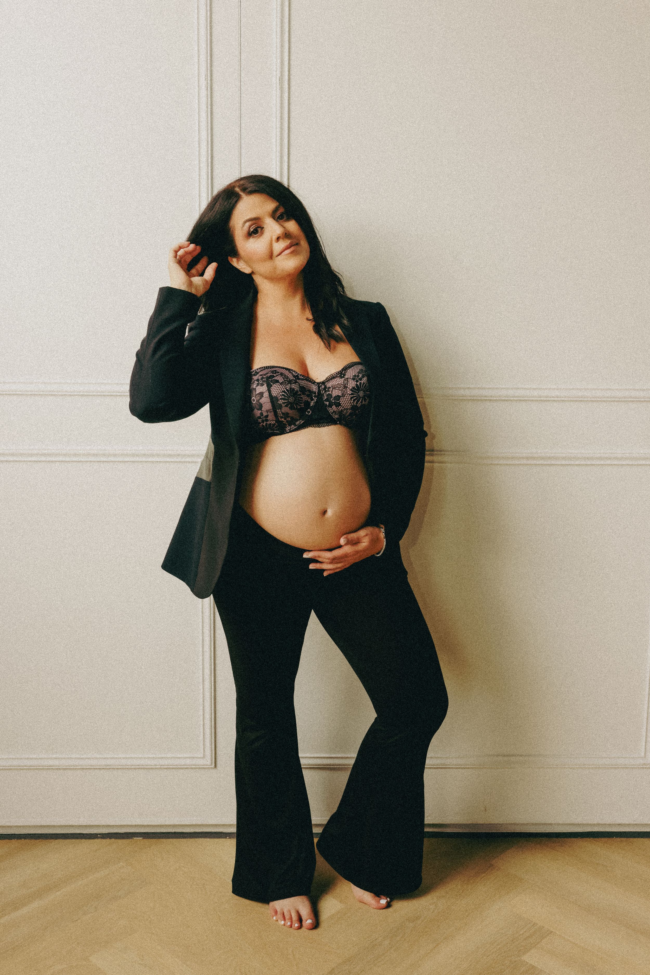 A maternity photo featuring a casual pose against a white paneled wall.