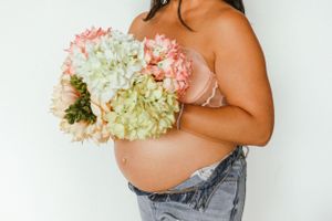 A maternity photo featuring a baby bump and a bouquet of pink and white hydrangeas.