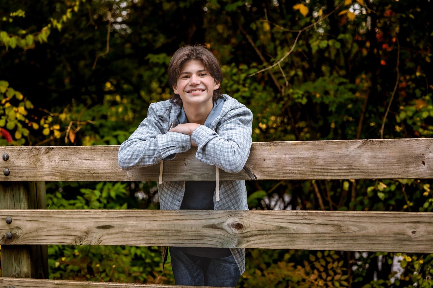 Person in grey hoodie leaning on wooden railing of outdoor bridge or deck.