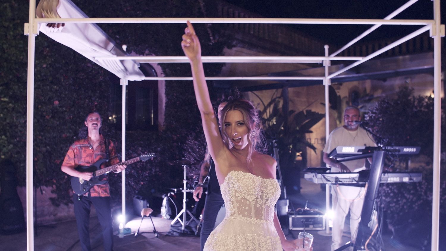 Wedding celebration with the bride dancing under a white tent with band performing in background.