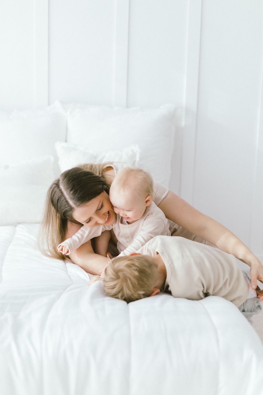 A tender moment of cuddles and bonding on white bedding in a bright minimalist setting.