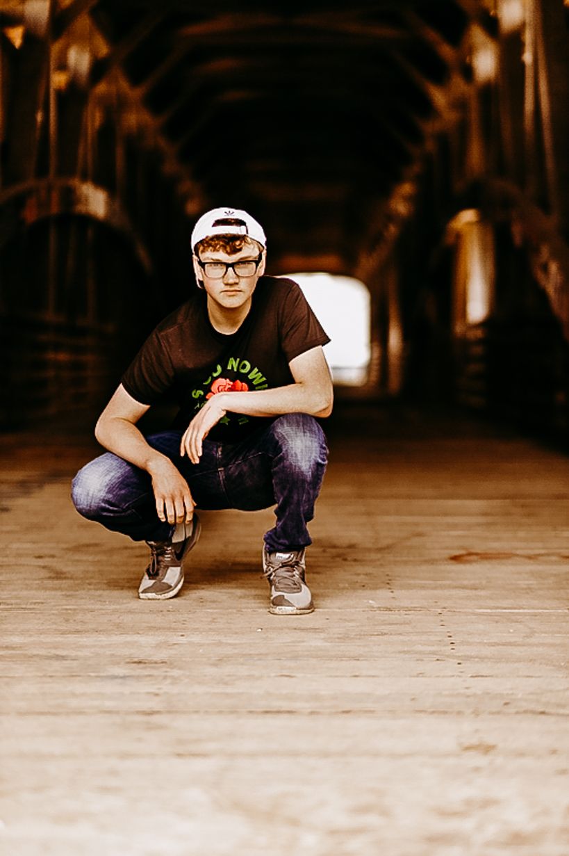 Person in baseball cap and Go North shirt crouching in wooden tunnel.