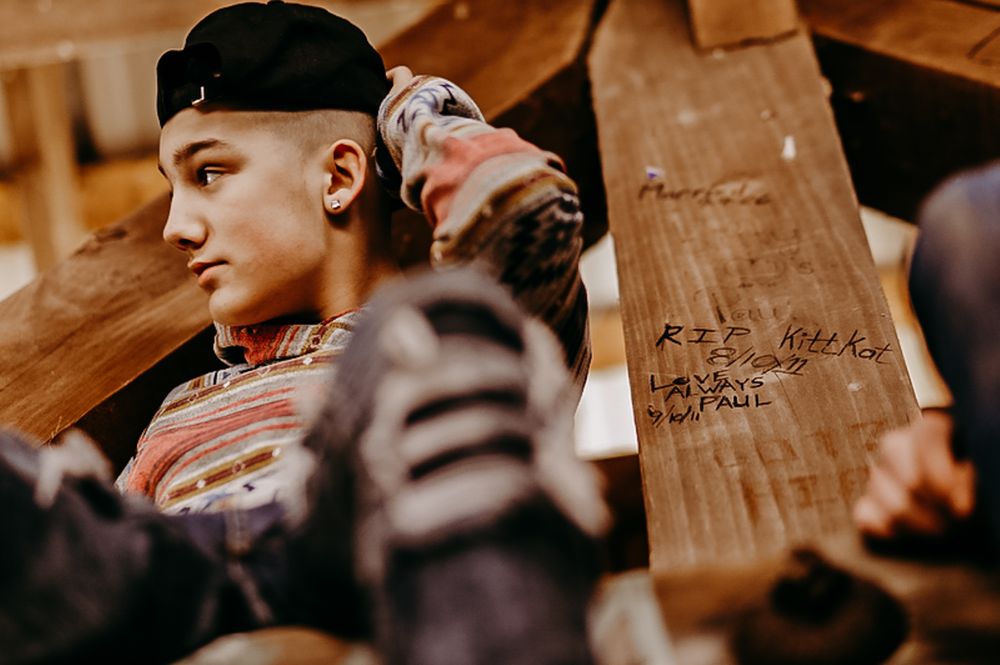 Person in baseball cap and striped sweater posing against wooden backdrop.