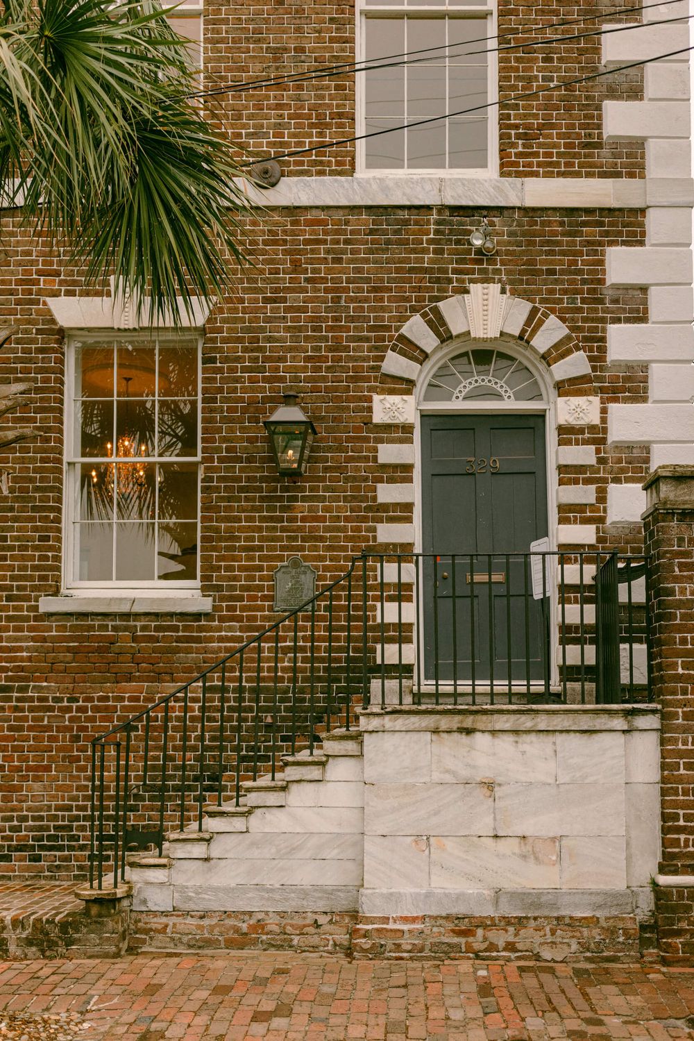 Historic brick townhouse with a distinctive arched doorway, iron railings, and palmetto tree in Charleston.