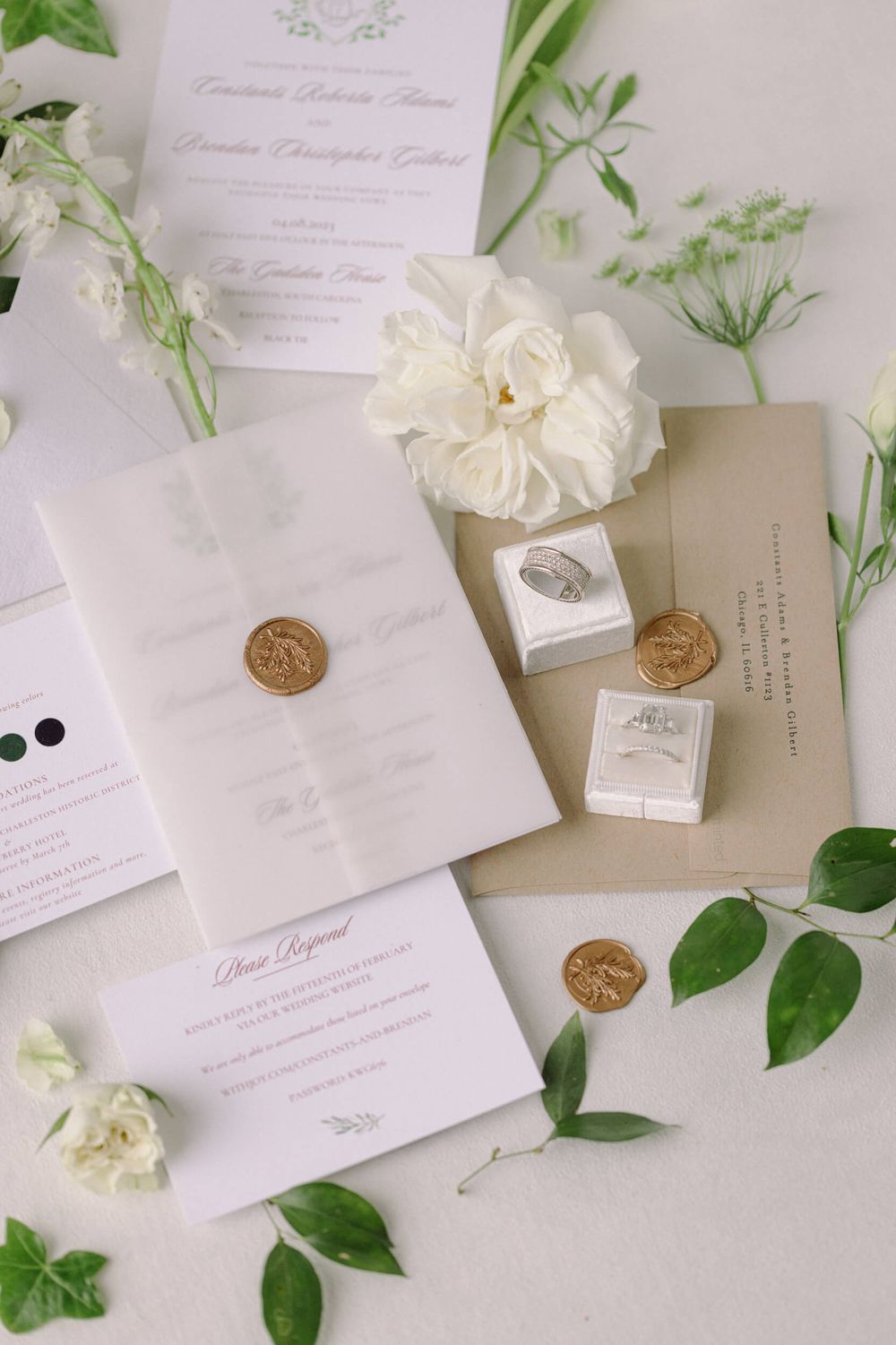Elegant wedding invitations with white florals, wax seals, and delicate greenery arranged on a light backdrop.