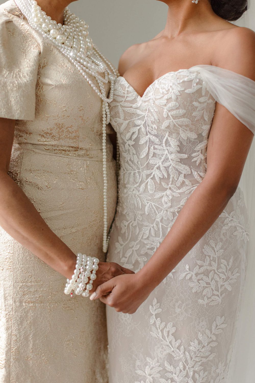 Close-up of two wedding dresses showing intricate lace details and pearl accessories.