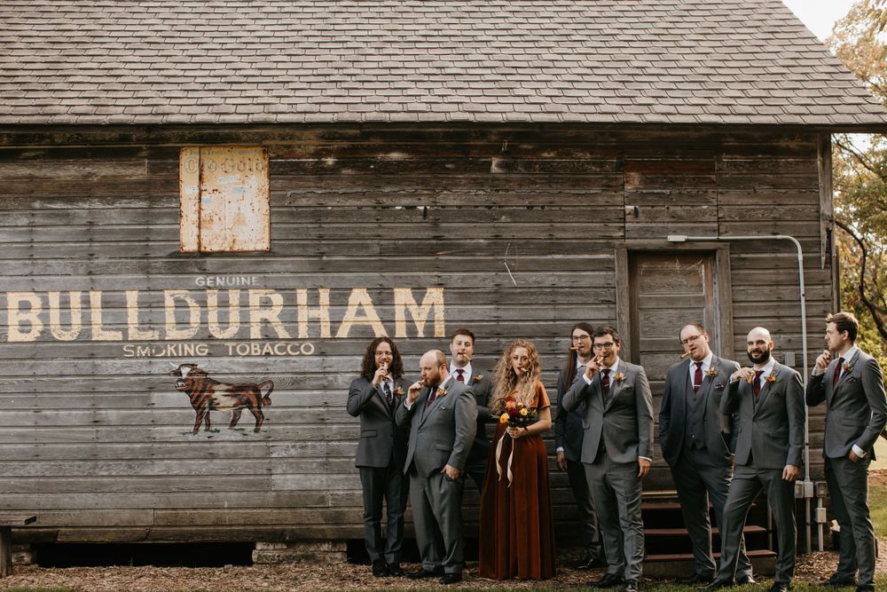 Wedding party poses beside vintage Bull Durham tobacco advertisement on rustic barn wall.