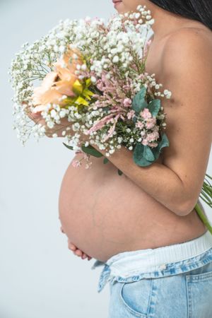 Close up of pregnant belly with floral bouquet featuring baby's breath and pastel blooms.