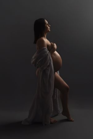 Dramatic maternity portrait with flowing fabric in moody studio lighting.