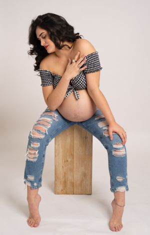 A maternity portrait featuring distressed jeans and a checkered top against a light background.